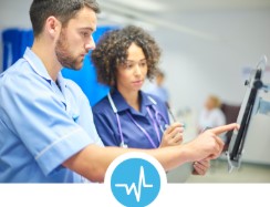 A man and a woman, both dressed in clinical uniforms, looking at a tablet screen together