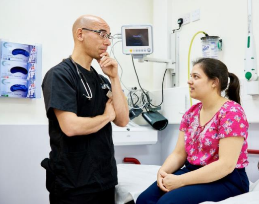 a female patient sat on an examination table, and a male doctor listening to what she is saying